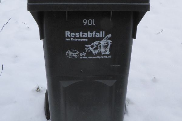 Eine schwarze Restabfalltonne steht mitten im Schnee.